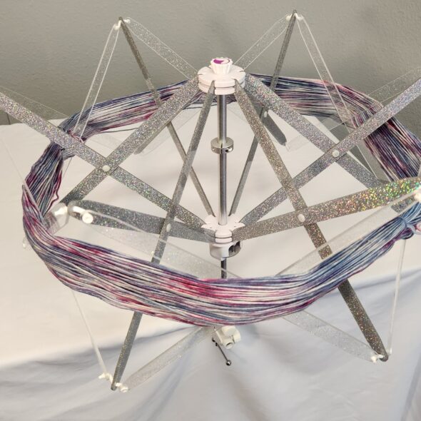 Alpenglow Glider Swift in Silver Rainbow—silver glitter arms with clear straps, yarn on the swift.
